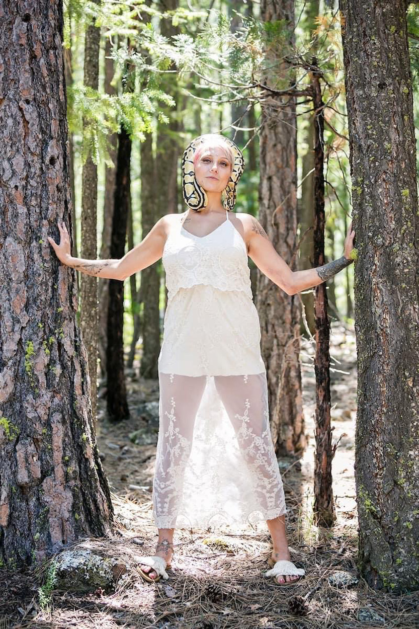 Woman in white dress standing amongst trees with arms outstretched.